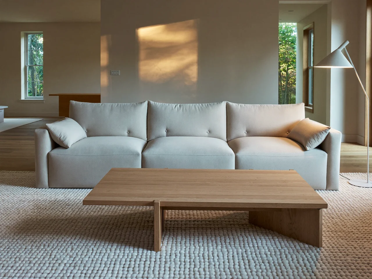 Wohnzimmer mit tiefem Sofa, Wollteppich, Eichentisch und Stehleuchte am Abend (Illustration)